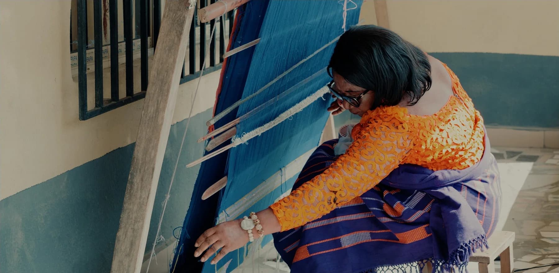 A weaver in Akwete working a wide blue cloth on the upright loom
